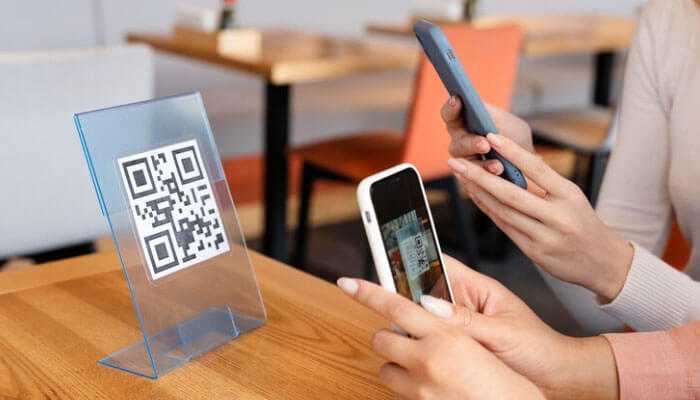 Utilizing qr codes for interactive content - tycoonstory | tycoonstory media Entrepreneurs using smartphones to scan a qr code on a table stand in a modern cafe, highlighting entrepreneurial success with qr codes.