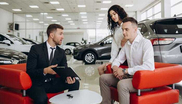 Whats included in the sale - tycoonstory | tycoonstory media A car salesman discussing buying a used car with a young couple in a dealership showroom