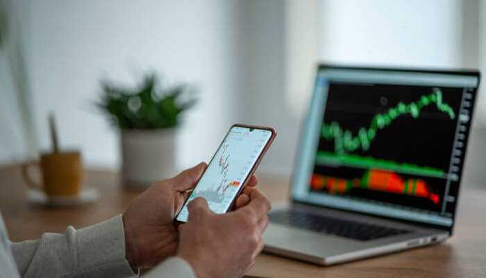 Building a strong dividend portfolio - tycoonstory | tycoonstory media Person analyzing stock market charts on a smartphone and laptop, reviewing market trends related to dividend stocks.