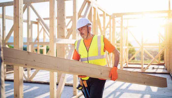 Construction speed - tycoonstory | tycoonstory media Construction worker carrying a wooden beam at a timber-frame construction site, showcasing the strength and sustainability of this modern building method.
