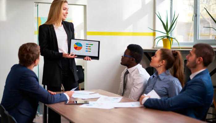 Data quality tycoonstory 1 | tycoonstory media A business professional presenting data quality indicators on a tablet to a team in a meeting. Colleagues discuss visual charts and metrics for data accuracy and consistency.