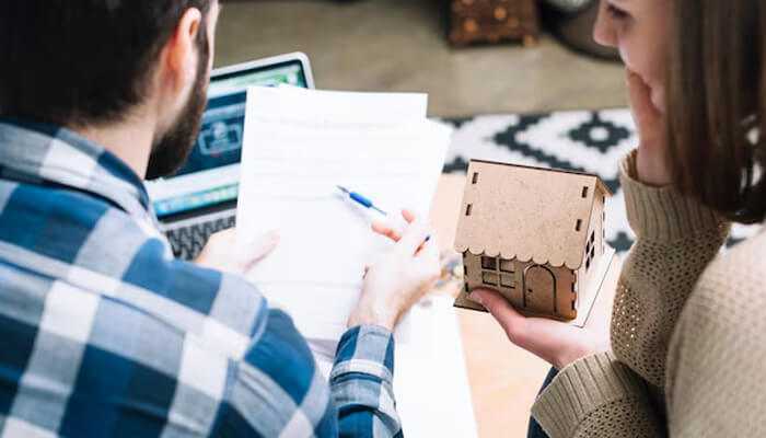 Evaluating property condition - tycoonstory | tycoonstory media Couple reviewing documents while holding a miniature house, symbolizing a smart investment in real estate.