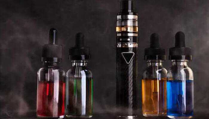 Factors impacting how long vape juice lasts in a device | tycoonstory media Various vape juice bottles in different colors alongside a vape device, surrounded by vapor, illustrating the question:'How Long Does Vape Juice Last?'