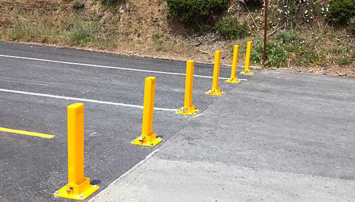 Flexible security for different needs - tycoonstory | tycoonstory media Bright yellow fold down bollards installed in a parking lot, providing secure and flexible access control. Ideal for preventing unauthorized vehicle entry.