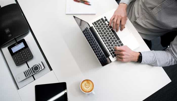 How essay services - tycoonstory | tycoonstory media A student entrepreneur working on a laptop at a modern workspace, with a cup of coffee and office essentials on the desk.