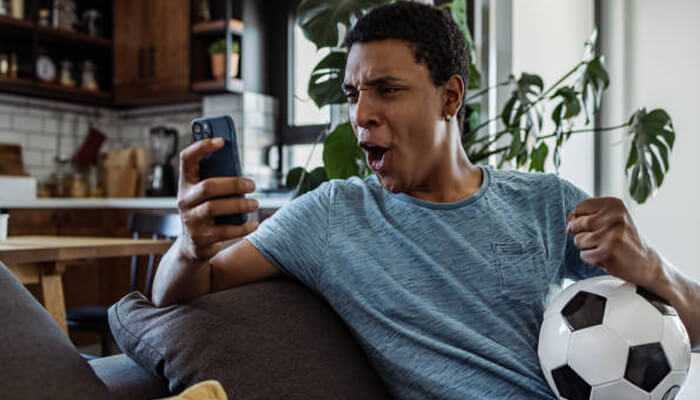 How to choose the ideal operator among all non gamstop bookmakers - tycoonstory | tycoonstory media Excited man holding a soccer ball and checking his phone, celebrating a win on an offshore betting sites.