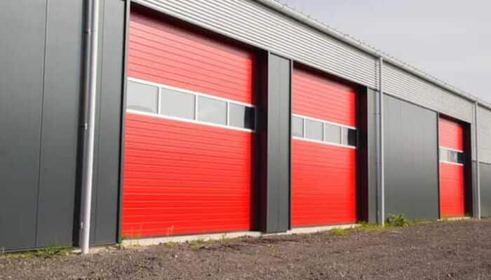 Improved energy efficiency and security - tycoonstory | tycoonstory media Exterior view of a warehouse featuring modern industrial doors in bold red, equipped with insulated panels and windows for enhanced energy efficiency and security.