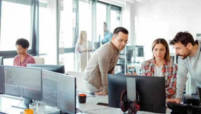 Our criteria for selecting the top custom software development companies in 2025 - tycoonstory | tycoonstory media Custom software development companies at work as a professional development team collaborates around computer screens in a modern office environment.