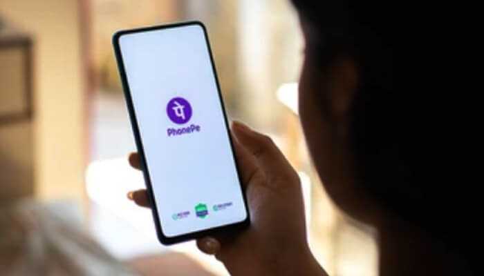 Phonepe - tycoonstory | tycoonstory media A person holding a smartphone displaying the phonepe app logo on the screen, which supports upi bill payments, with a blurred background.