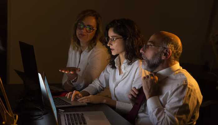Stealth startup - tycoonstory | tycoonstory media A team working late in a dimly lit office, strategizing on their stealth startup plans while collaborating on laptops.