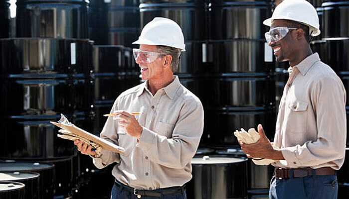 Train employees on safe handling and storage - tycoonstory | tycoonstory media Two workers in safety gear inspecting storage barrels for storing hazardous materials.