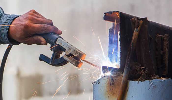 Tungsten electrodes 1 | tycoonstory media A worker welding metal with a handheld tool, emphasizing the role of handheld tungsten grinders for precise electrode preparation. "