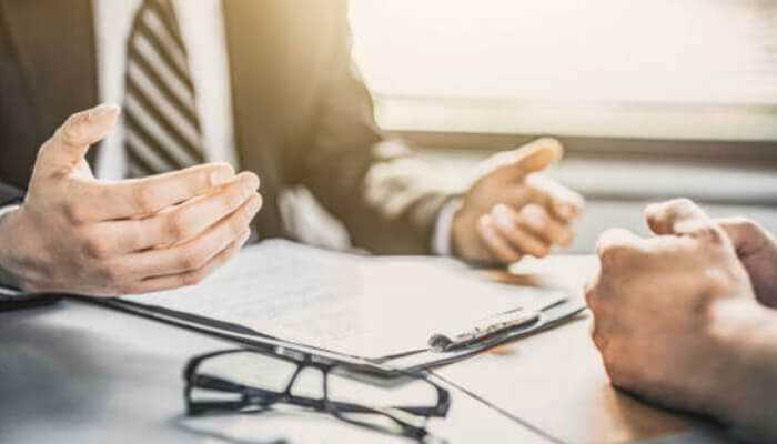 Types of consumer loans - tycoonstory | tycoonstory media Close-up of a financial consultation about consumer loans, showing hands gesturing over loan documents on a desk with a pen and glasses.