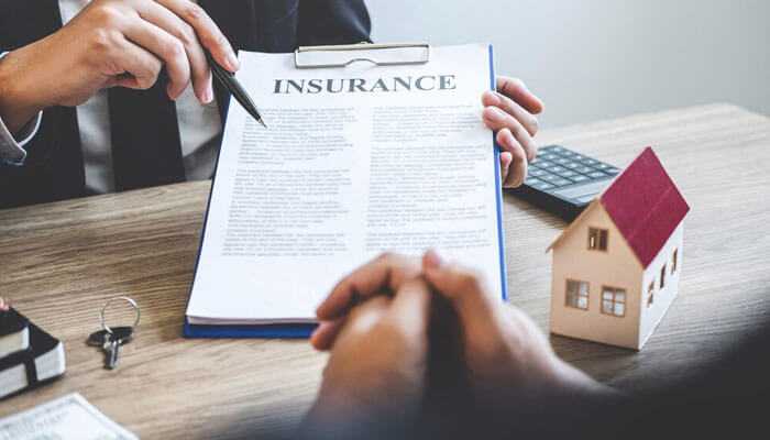 All home insurance policies are the same - tycoonstory | tycoonstory media People reviewing and signing an insurance policy beside a house model, highlighting home insurance myths related to policy terms and coverage limits.