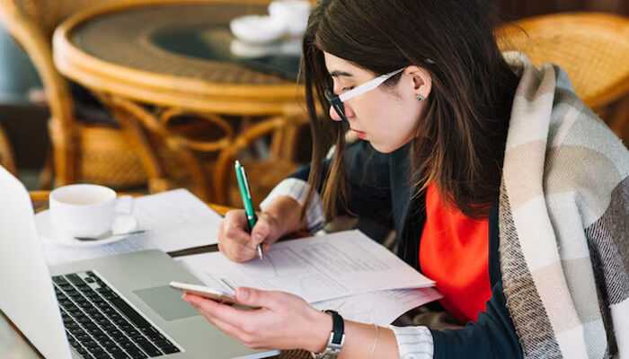 Avoiding unreliable sources | tycoonstory media A focused student researching on a laptop while taking notes, ensuring she gathers reliable information for essays from credible sources.