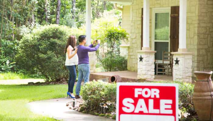 Buyers look for signs of care | tycoonstory media A couple poses in front of a house with a for sale sign, showcasing elements that what homebuyers really notice.