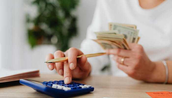 Choose the right lender | tycoonstory media A woman holding cash and using a calculator to manage personal finances—analyzing the real pros and cons of debts and exploring debt consolidation options.
