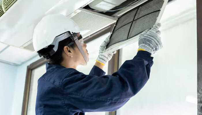 Energy efficiency and hvac longevity | tycoonstory media A man in a hard hat and safety glasses works on an air conditioner, highlighting the importance of air duct cleaning.