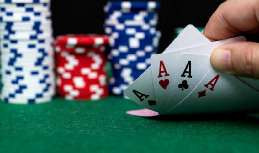 Four of a kind | tycoonstory media Poker hand with four aces being held against poker chips, representing a strong hand in the game of poker.