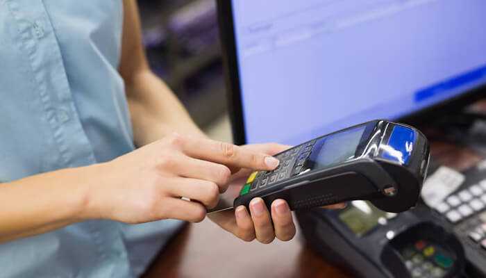Payment | tycoonstory media A person using a payment terminal to process a transaction in a retail setting.