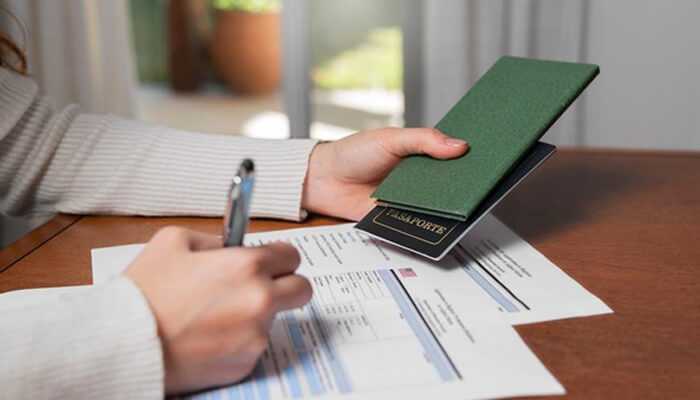 Signs you should hire a green card lawyer immediately | tycoonstory media Person filling out immigration forms with a passport in hand — green card lawyer assistance concept.