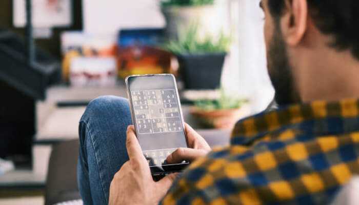 Solo game | tycoonstory media Man playing a puzzle game on his phone as one of his favorite solo activities at home
