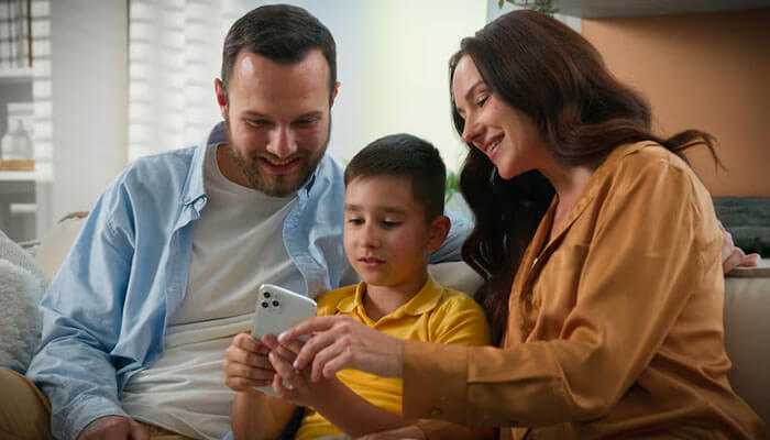 Teach respect for others online - tycoonstory | tycoonstory media Parents guiding their young son on responsible cell phone use at home, highlighting positive family tech interaction.