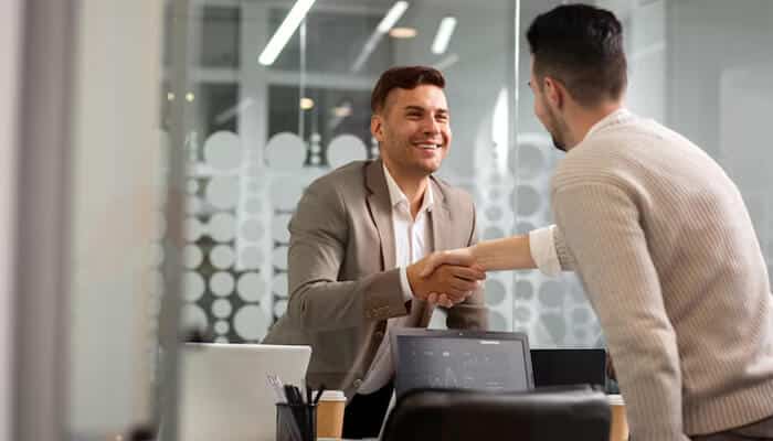 The unseen standard of excellence in corporate chauffeur services | tycoonstory media Two professionals smiling and shaking hands in a modern office, representing positive communication and trust—key elements of client satisfaction.