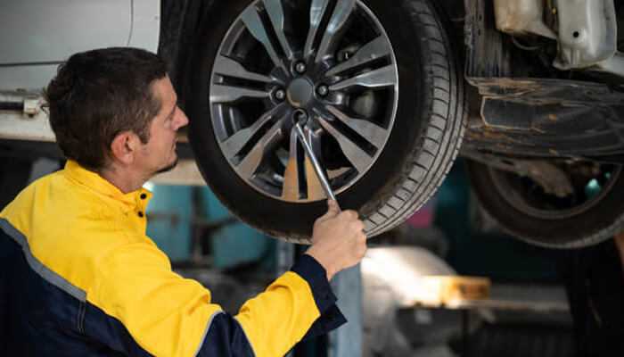 Tire condition and suspension safety | tycoonstory media A man in a yellow jacket performs maintenance on a car at full-service auto repair.