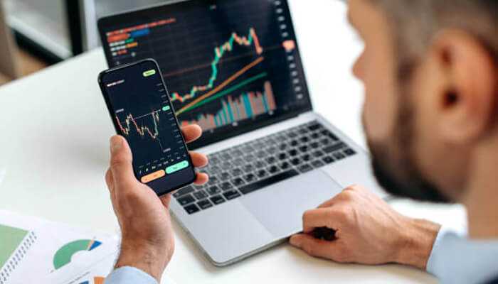 A leading share trading app for smart investing | tycoonstory media Man analyzing stock market data on his smartphone and laptop, using the samco share trading app to make informed investment decisions.