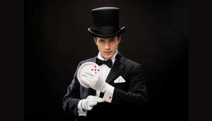 Aaa | tycoonstory media A man dressed in formal poker style, wearing a top hat, tuxedo, and white gloves, demonstrating card tricks with a deck of playing cards.