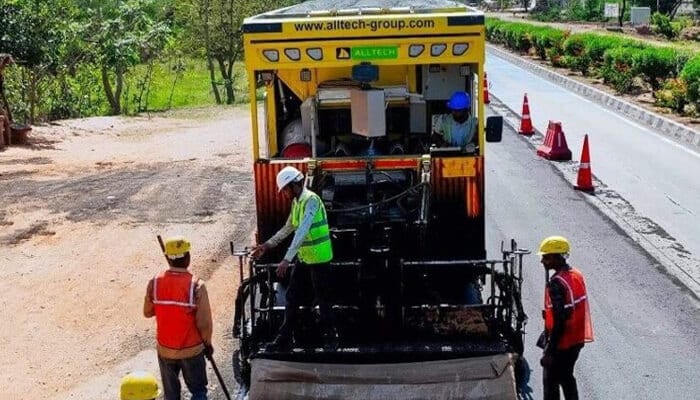 Alltech | tycoonstory media Alltech mobile asphalt batch mix plant machine in operation on a road project with workers wearing safety helmets and vests.