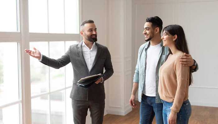 Application across different client segments | tycoonstory media Real estate agent showing a property to a young couple — generating quality leads in real estate through personal interaction.