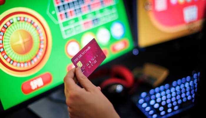 Casino policies and internal processing times | tycoonstory media Person holding a credit card in front of a computer screen displaying an online roulette game, representing secure online transactions for the online casino best payout.