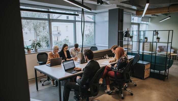 Collaboration without the noise | tycoonstory media A team collaborating around a large table in a well-designed office with modular furniture, supporting flexible work environments and team interaction.