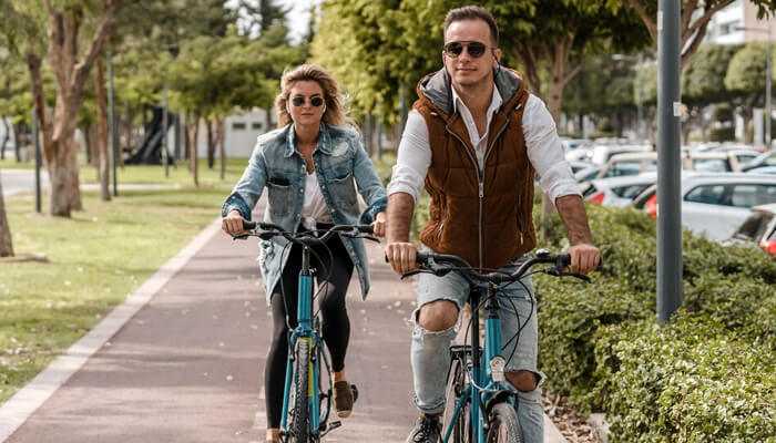 Ebike 2 | tycoonstory media A couple riding e-bikes on a paved path surrounded by greenery, showcasing a relaxed and eco-friendly way to travel.