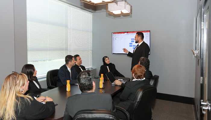 Engineer ahmad ayoubipour | tycoonstory media Ahmad ayoubi pour leading a professional business meeting in a conference room, addressing a diverse team with a presentation on a digital screen.