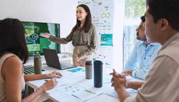 Key technologies that drive sustainability industry 4 1 | tycoonstory media Team collaborating in an office setting presenting data on a screen, illustrating sustainable business transformation strategies.