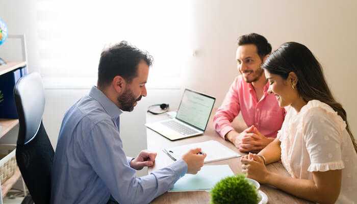 Loan | tycoonstory media Couple meeting with a real estate agent to discuss options for apartments for sale, reviewing documents and loan agreements to purchase their first home.