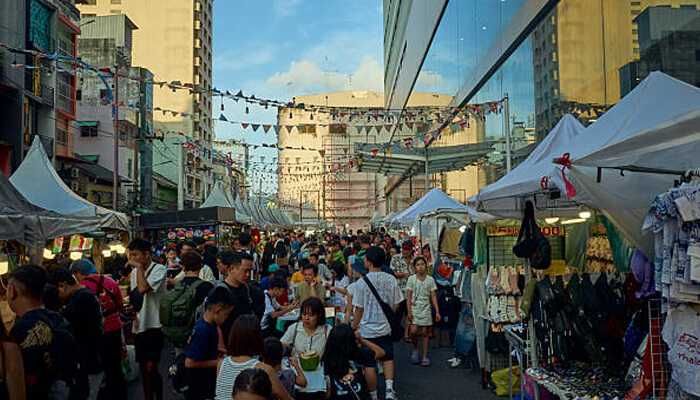 Outdoor retail pop-ups | tycoonstory media A bustling outdoor market with heavy-duty canopy tents set up along the street, showcasing vibrant retail booths and large crowds of shoppers.