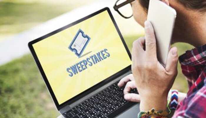 Real-world uses of sweepstakes games | tycoonstory media Person participating in sweepstakes games, viewing a laptop screen with the word'SWEEPSTAKES' on it while holding a smartphone in hand.