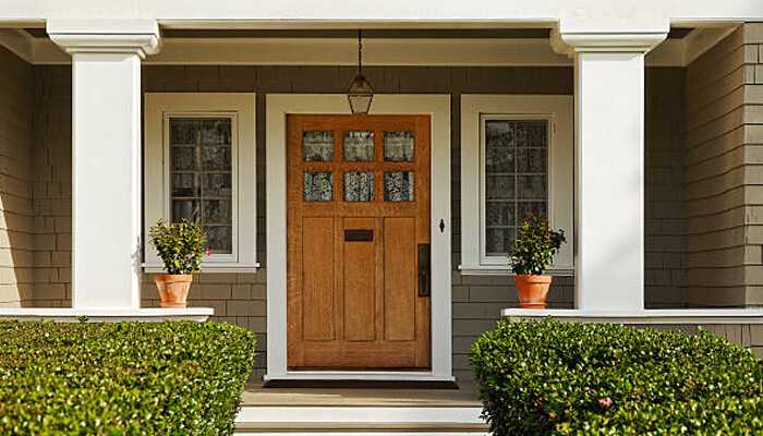 Refresh the front door and entryway | tycoonstory media Freshly painted wooden front door with potted plants and trimmed hedges — a great example of curb appeal tips to enhance your home’s entryway.