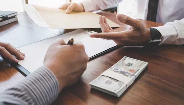 Research markets thoroughly to support your idea | tycoonstory media A businessperson signing an agreement with a stack of cash on the table, symbolizing the process of securing a startup loan for new ventures.