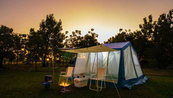 Sheltered eating and sitting areas | tycoonstory media Comfortable outdoor setup with chairs, firepit, and spacious tent under a glowing sunset, highlighting the appeal of modern camping accommodations with relaxing amenities.