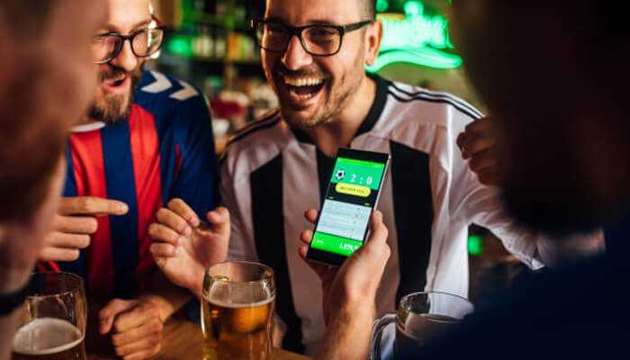 Use odds comparison tools | tycoonstory media Group of friends celebrating while viewing live betting results on a smartphone, highlighting excitement after placing spot value bets during a game.