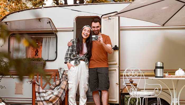 Using your motorhome as a permanent residence | tycoonstory media Happy couple posing outside their motorhome set up as a cozy living space, illustrating lifestyle choices that may lead to motorhome insurance exclusions for full-time residence use.