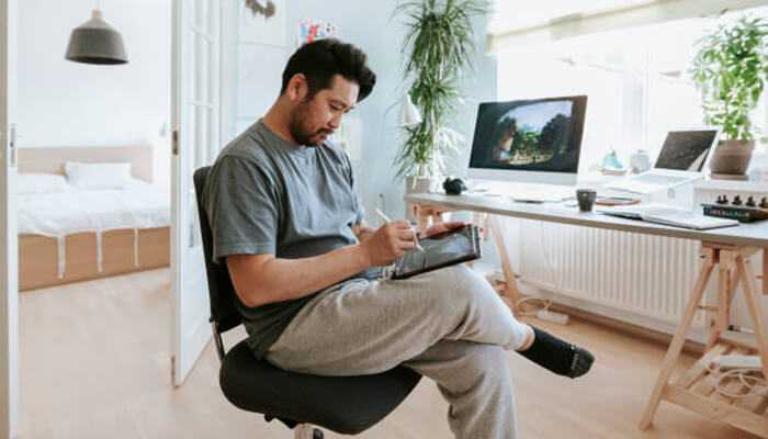 Wear dress sweats | tycoonstory media Man working on a tablet in a modern home office, dressed in comfortable clothing ideal for productivity at home.