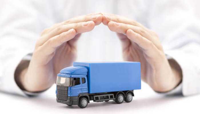 What affects the premium of a truck insurance policy | tycoonstory media Hands protecting a blue delivery truck model — symbolizing coverage and protection offered by commercial vehicle insurance policies.