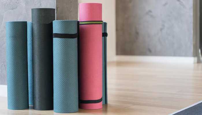 Best thickness for different workouts | tycoonstory media Multiple rolled-up gym floor mats in various colors neatly stored against a wall in a home or studio fitness space.