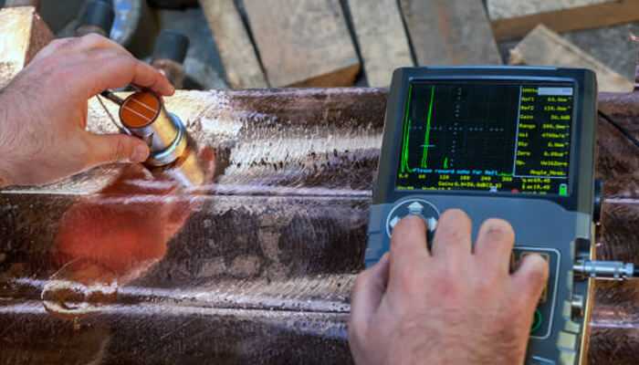Confidence through consistency | tycoonstory media Technician performing ultrasonic non-destructive testing (ndt) on a metal weld using a handheld transducer and diagnostic screen.